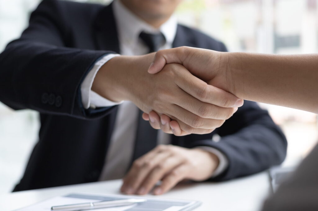 Two people shaking hands over a table in the context of hiring process servers.